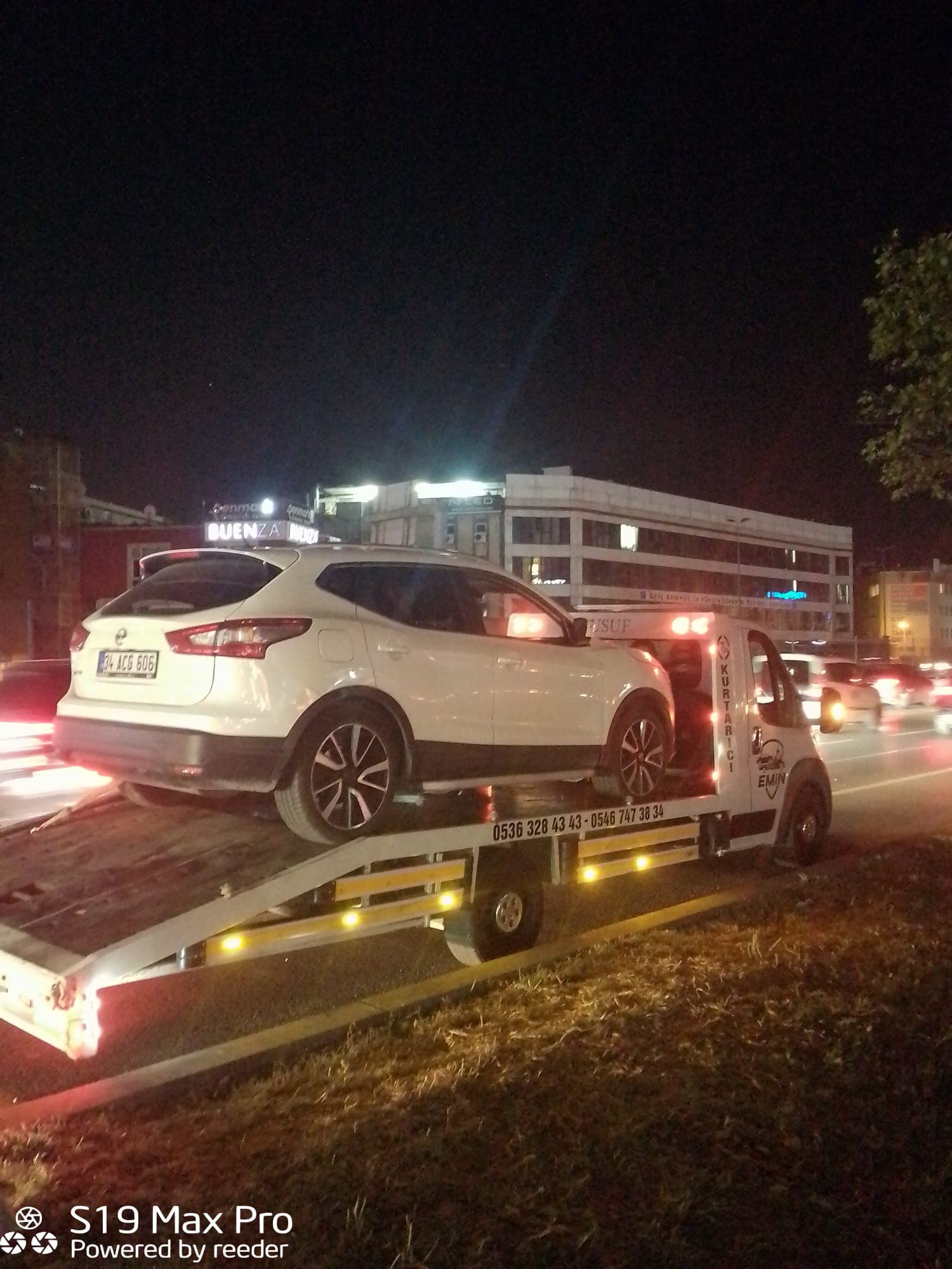 Emin Oto Kurtarma çekicisi gece şehir içinde beyaz bir SUV taşırken, platform üzerindeki sarı ikaz lambaları yanıyor